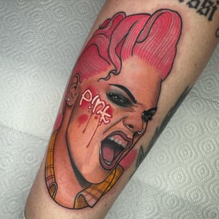 Colorful portrait tattoo of a person with pink voluminous hair, open mouth expression, and yellow plaid clothing on the forearm.