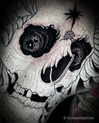 Skull tattoo with floral ornamental details and decorative elements on skin, rendered in black ink with shading and linework.