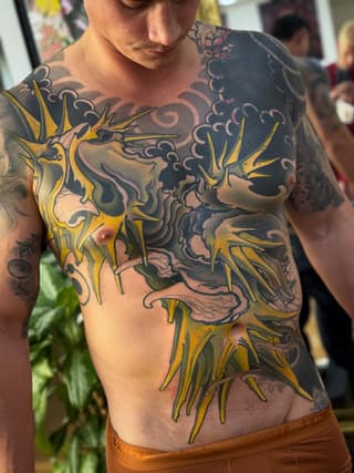 Chest and torso tattoo featuring yellow sunflowers with dark ornamental scrollwork and floral designs in black and purple ink.