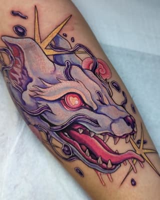 Colorful demon or dragon head tattoo on forearm featuring purple, red, and gold tones with sharp teeth, glowing eye, and decorative horns.