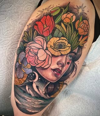 Colorful shoulder tattoo of a woman's face with flowing hair and flowers blooming from her head, featuring red, orange, and yellow blooms with green foliage.