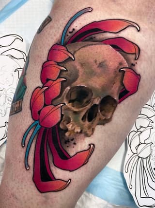 Colorful tattoo on upper arm featuring a skull with red flower petals and blue antennae surrounding it, displayed on light skin.