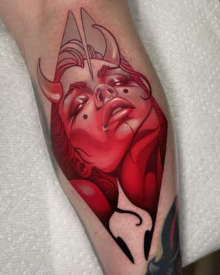 Red and black portrait tattoo of a demon face with horns on the calf, featuring detailed shading and anatomical features.