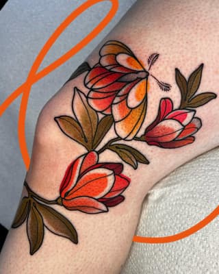 Colorful floral tattoo on the upper arm featuring red, orange, and yellow flowers with brown leaves and black line work.