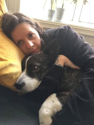 Woman with a dark curved line tattoo on her upper arm, sitting with a husky dog by a sunny window.