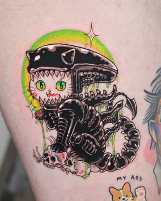 Colorful cat with sharp teeth emerging from biomechanical alien xenomorph creature with green and yellow gradient background on upper arm.