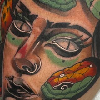 Colorful facial tattoo featuring green and red leaf designs, black eyeliner details, and orange-red butterfly motifs on the cheek and forehead area.