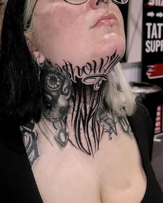 Large-scale neck and chest tattoo featuring an eye, flowing script text, and ornamental designs in black ink on pale skin.