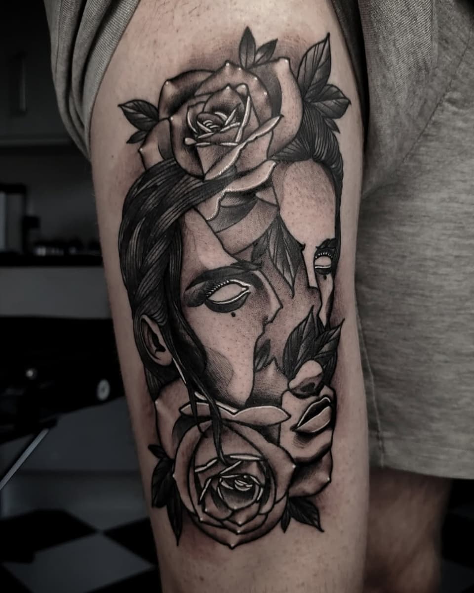 Tattoo on thigh featuring an abstract face with closed eyes, long hair, and roses integrated into the design in black ink on skin.