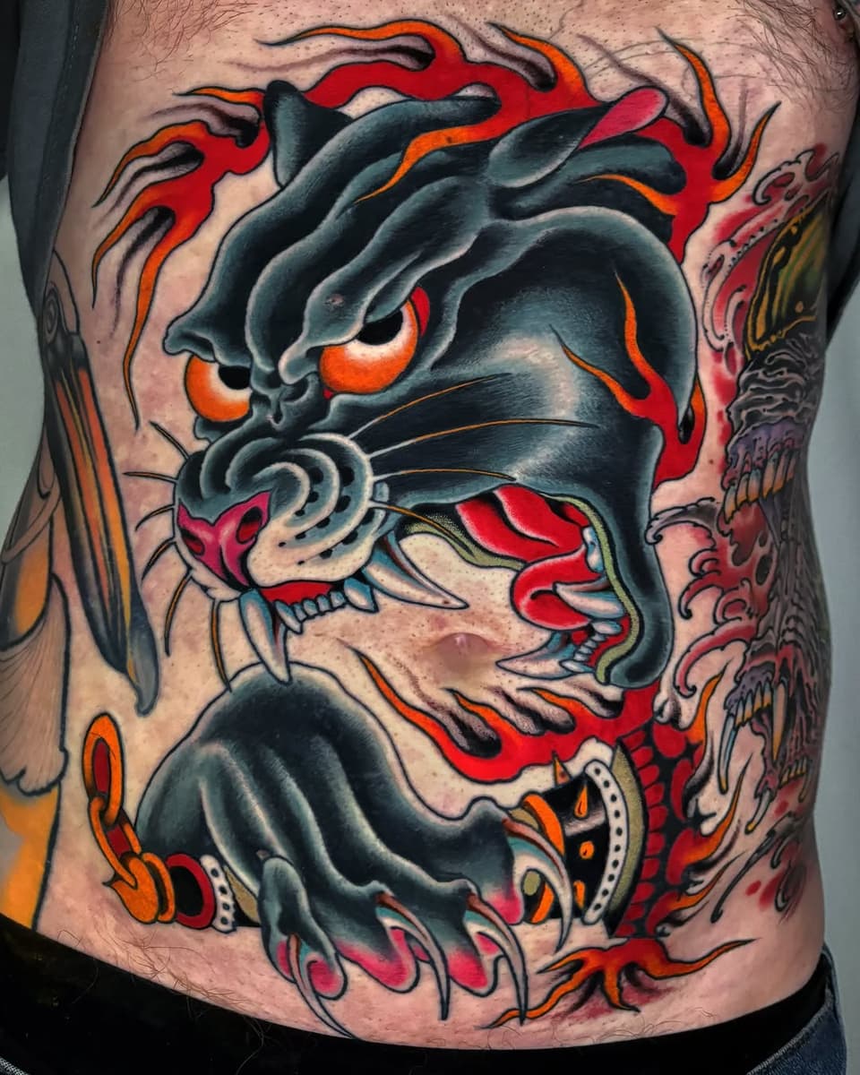 Demonic face tattoo with glowing orange eyes, red flames, sharp teeth, and decorative elements in black, red, orange, and gray on the chest.