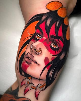 Colorful tattoo on a calf featuring a female character with black hair, red face makeup, orange eyes, and orange circular elements, against an orange background.
