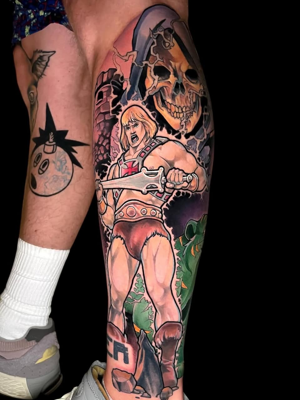 Colorful leg sleeve tattoo featuring a muscular warrior with blonde hair holding an axe, skull imagery, and fantasy creatures in orange, green, and red tones.
