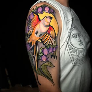 Colorful bird tattoo on upper arm featuring a cardinal with red and orange wings, yellow background, and purple flowering vine, surrounded by green foliage.