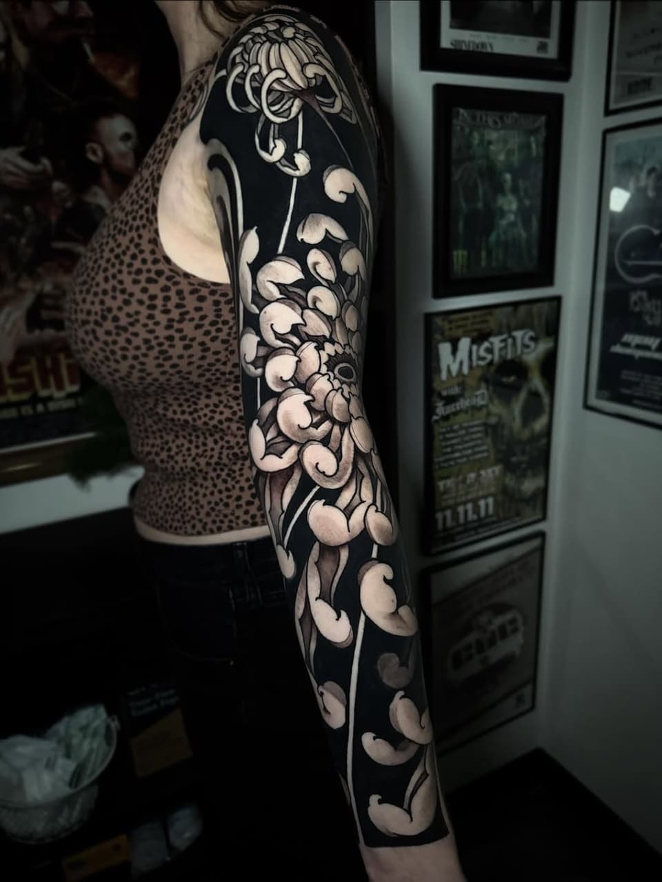 Full arm sleeve tattoo featuring ornamental floral and botanical designs with white highlights on black background, displayed on a person's left arm.