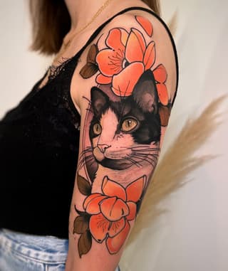 Black and white cat with golden eyes surrounded by orange and red flowers on the upper arm.