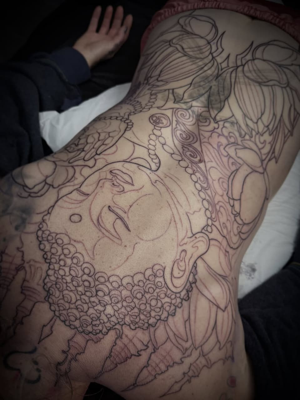 Large detailed tattoo on back and shoulder featuring a woman's face surrounded by ornamental flowers and decorative beading patterns in black ink.