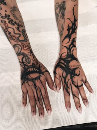 Extensive black ink hand and forearm tattoos featuring eyes, snakes, flowers, and abstract designs on a person with manicured nails.