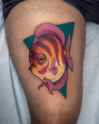 Colorful fish head tattoo on thigh featuring pink, orange, yellow, and red gradient scales with pink fins against a teal geometric triangle background.