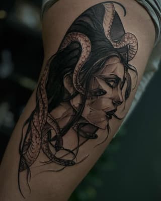 Profile of a woman's face with serpents wrapping around her head and neck, rendered in black and brown ink on the upper arm.