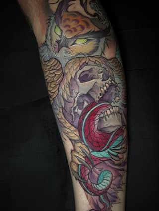 Colorful leg tattoo featuring a cat with yellow eyes at top, skull in center, and red flower with teal leaves at bottom.