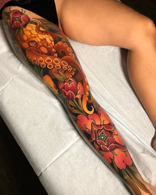 Full-sleeve arm tattoo featuring red and orange flowers, an octopus with detailed suction cups, ornamental scrollwork, and dark background fill on a person's arm.