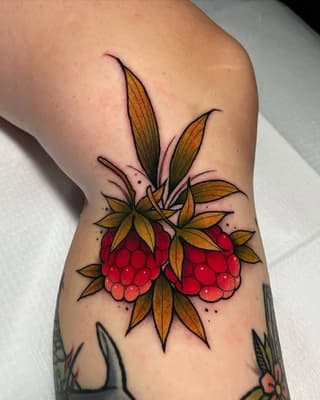 Two red raspberries with golden-orange leaves and thin black outlines on the inner forearm, surrounded by small decorative dots.