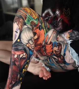 Colorful full-sleeve tattoo featuring cartoon characters including a masked face, grinning creature, and orange-clad figure with vibrant reds, yellows, greens, and blues.