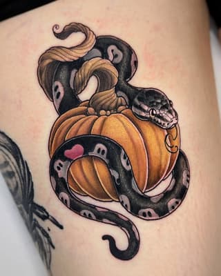 Colorful tattoo on upper arm featuring coiled snakes intertwined with orange pumpkins and small skull details, with pink accents throughout.