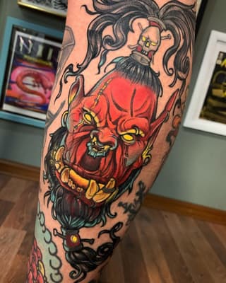 Colorful leg tattoo featuring a demon face with red skin and yellow eyes below a woman with flowing dark hair and skull face paint.