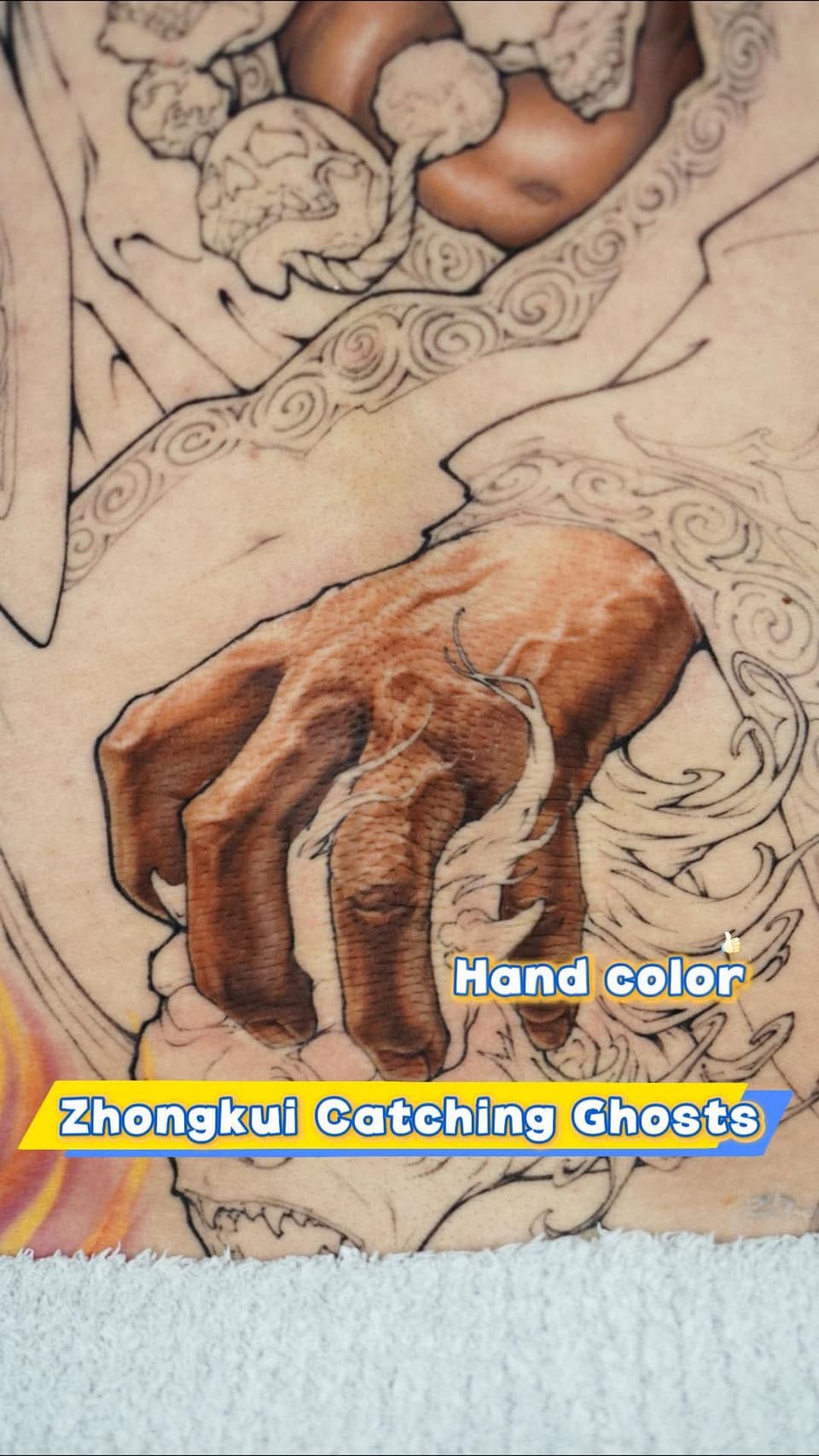 Colored hand tattoo featuring a brown fist with white highlights surrounded by decorative spiral patterns in tan and black outlines.