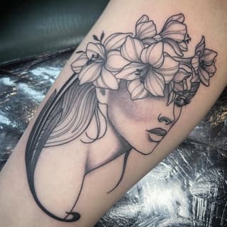 Woman's profile with flowing hair and delicate flowers crowning her head, rendered in black ink on arm skin.
