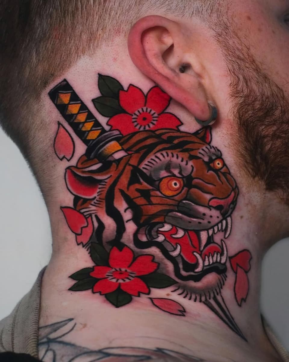 Colorful fish head tattoo with red flowers and black leaves on a person's neck, featuring orange and black striped details.