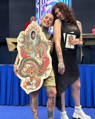 Two people on stage display a large dragon illustration in red, gold, and cream colors with an ornate temple design below it.
