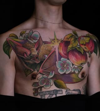 Colorful chest tattoo featuring a bat with flowers, pomegranates, a glowing star, and decorative scrolls in reds, yellows, purples, and greens.
