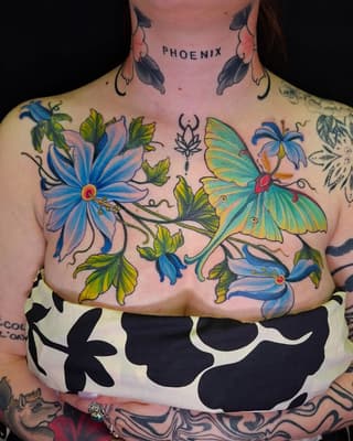 Colorful chest tattoo featuring blue flowers, a green and yellow butterfly, botanical elements, and "PHOENIX" text on the neck.