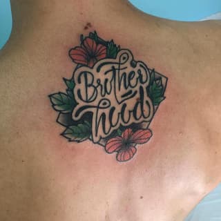 Shoulder tattoo featuring "Brother Till" script lettering surrounded by green leaves and red-pink flowers on tan skin.
