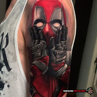 Close-up shoulder tattoo featuring a red and black masked character with studded gloves and belt, displayed on bare skin.