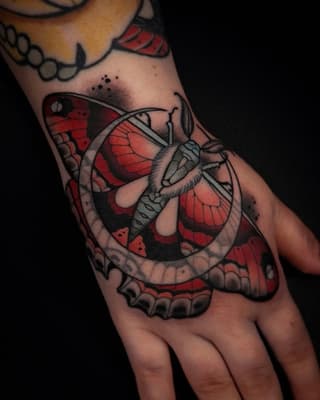 Detailed butterfly tattoo on hand featuring red and black wings with intricate line work and shading on the palm and fingers.