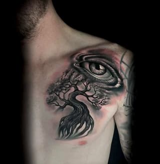 Detailed tattoo on chest featuring a large eye with a tree growing from below, rendered in black and gray with pink shading, positioned on male torso.