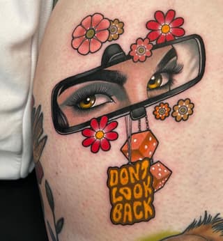 Colorful tattoo on upper arm featuring a woman's face in a phone mirror with flowers and dice, text reading "Don't Look Back" below.