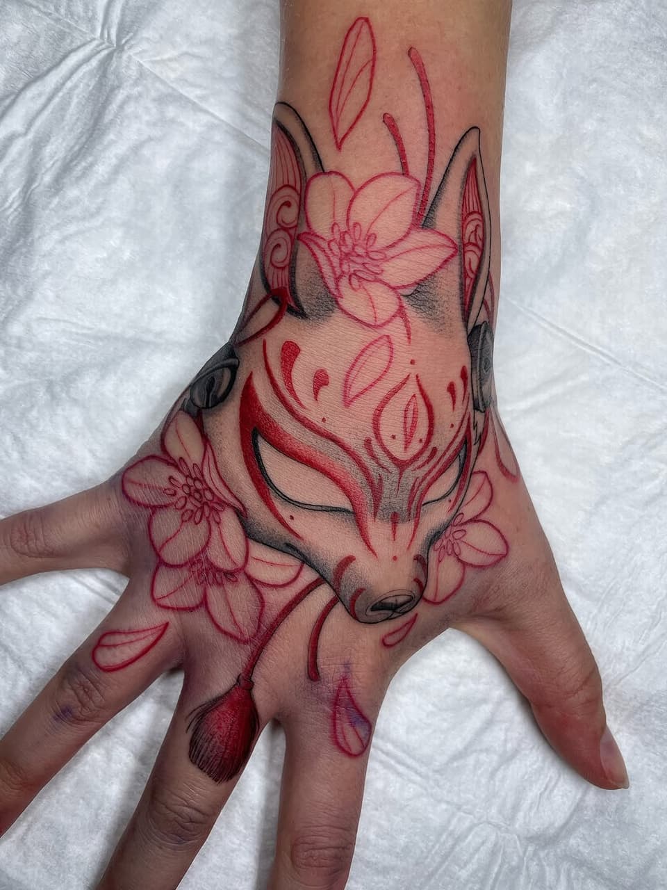 Red and black fox head with floral elements and decorative antlers on hand and wrist of a person against white fabric.