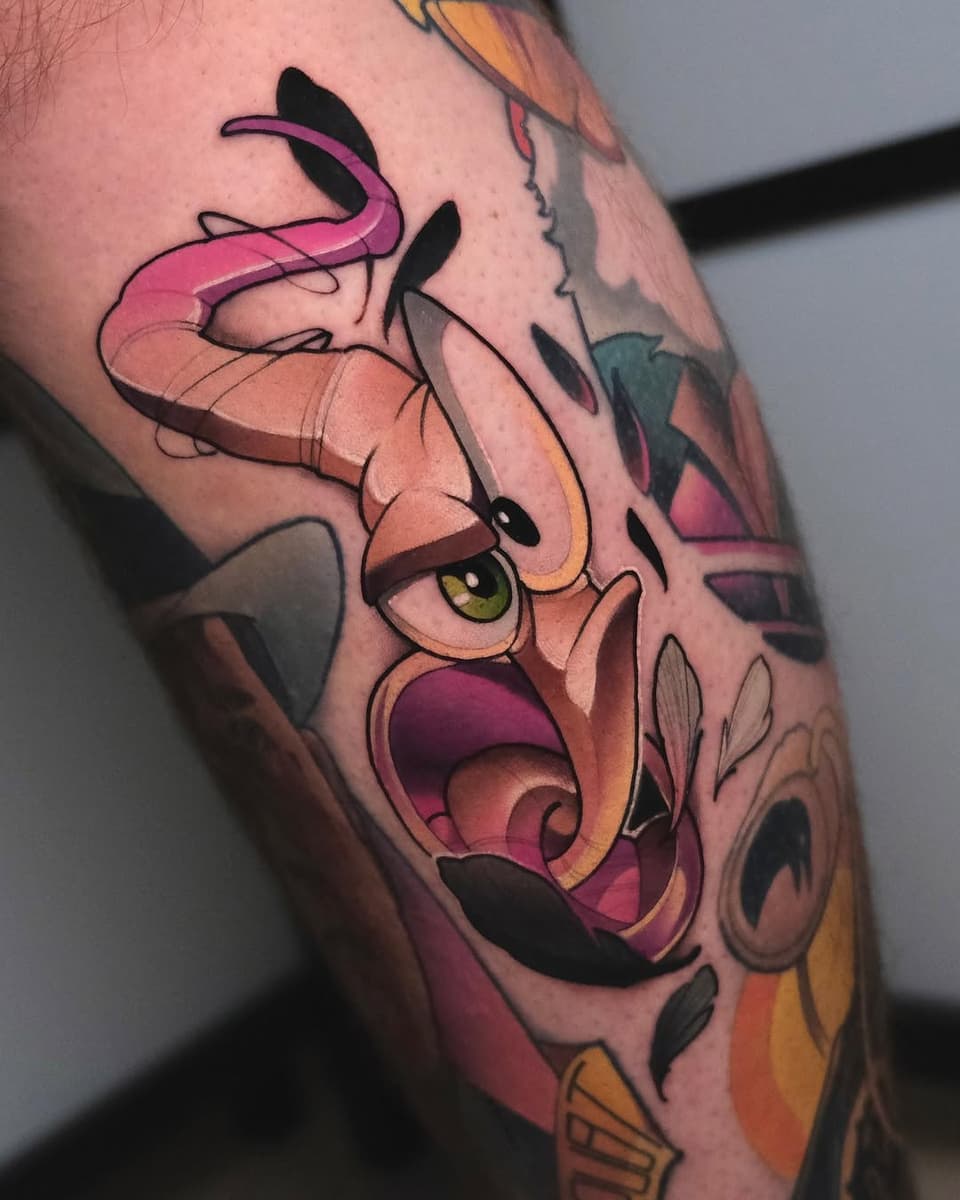 Colorful leg tattoo featuring an expressive character with pink tentacles, yellow eyes, and an open mouth in shades of orange, pink, and yellow.