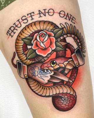 Colorful thigh tattoo featuring a coiled snake with horns, red rose, hands holding a knife, and text reading "Trust no one" in an arc.