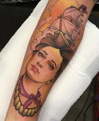 Colorful arm tattoo featuring a woman's portrait with flowing hair, ornate collar, and decorative elements in orange, purple, and yellow tones.