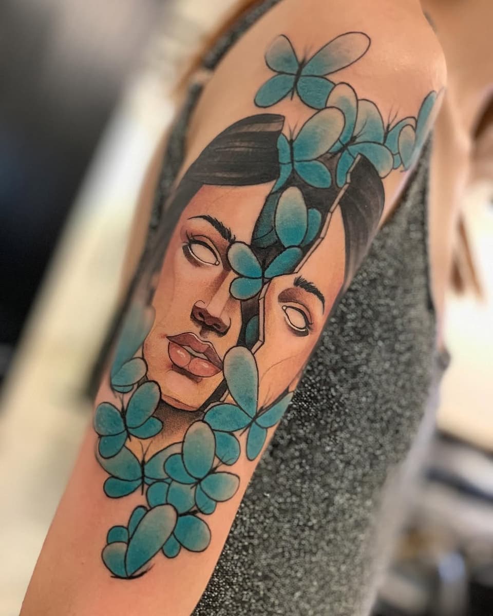 Colorful tattoo on an arm featuring a stylized face with closed eyes and full lips surrounded by turquoise four-leaf clovers and botanical elements.
