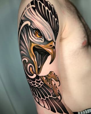 Detailed eagle head tattoo on upper arm featuring golden yellow eyes, black and gray plumage, and tan talons against pale skin.