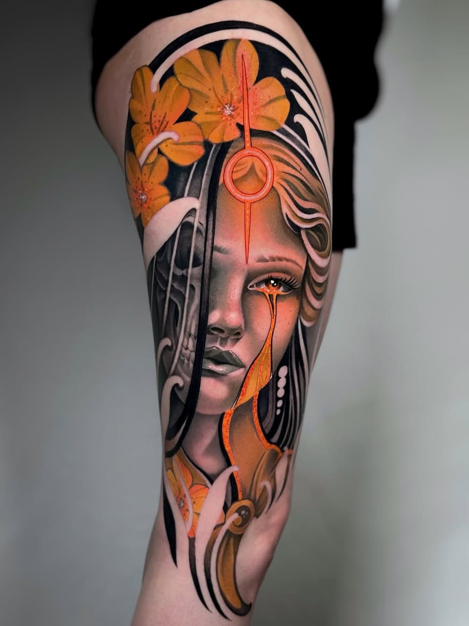 Portrait tattoo on thigh featuring a woman's face with orange flowers, geometric elements, and orange teardrops in orange, black, and skin tones.