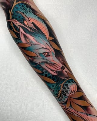 Colorful dragon and fox mask tattoo on forearm featuring teal, pink, gold, and bronze tones with scaled and feathered details.