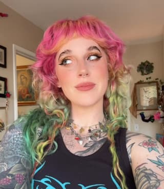 Portrait of a person displaying colorful floral and botanical tattoos on their arms and chest, wearing a black graphic t-shirt.