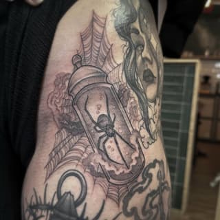 Spider web and spider design with portrait face on upper arm, rendered in black and gray ink with dotted shading details.